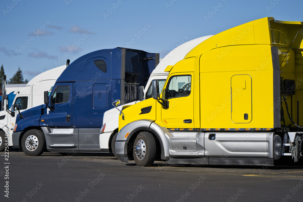 Bright big rig semi trucks standing in row on truck stop in sunny day