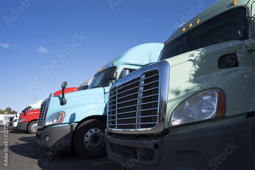 Cabs of big rigs semi trucks with grilles and headlight standing in row on truck stop © vit