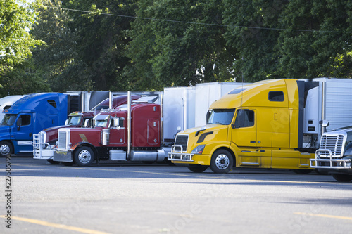 Fotografie, Obraz Different big rigs semi trucks with semi trailers standing in row on truck stop