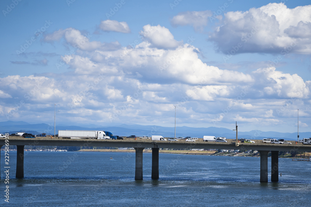 Long bridge across the Columbia River with heavy traffic of semi trucks and another cars on the background of cloudy sky