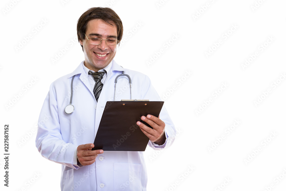 Studio shot of young happy Persian man doctor smiling while read Studio shot of young happy Persian man doctor smiling while read