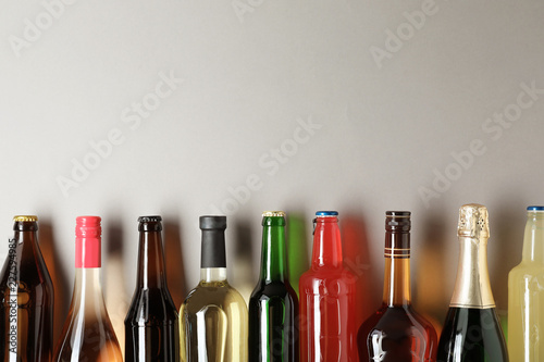 Bottles with different alcoholic drinks on light background, top view. Space for text