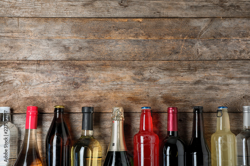 Bottles with different alcoholic drinks on wooden background, top view. Space for text