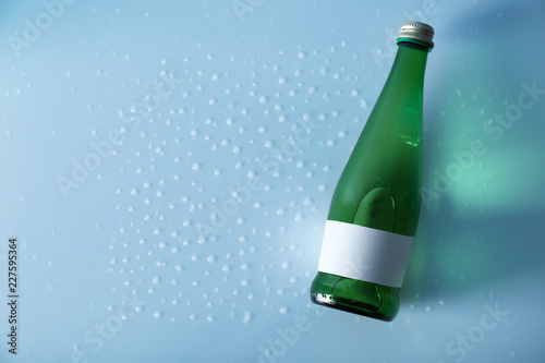 Bottle of water on wet light surface, top view. Space for text