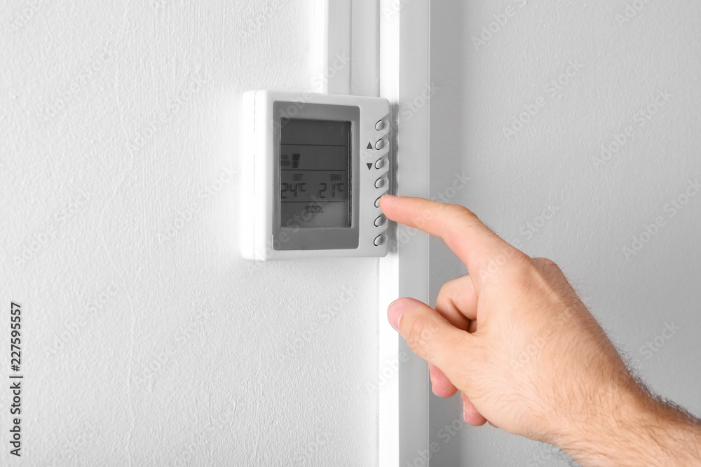 Man adjusting thermostat on white wall, closeup. Heating system Man adjusting thermostat on white wall, closeup. Heating system