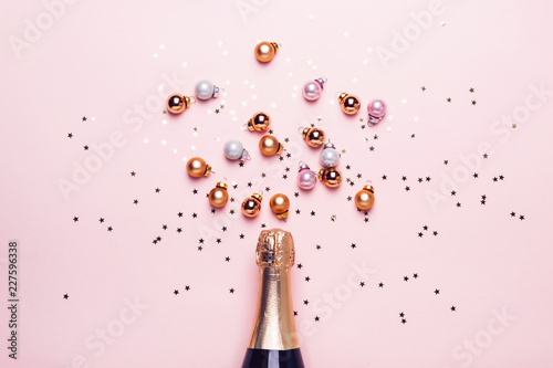 Canvas Print Champagne bottle and scattering of golden shiny balls and confetti on pink backg