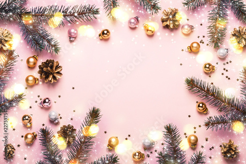 Pastel Pink Christmas Background. Festive frame of fir branches, toys and golden bokeh lights