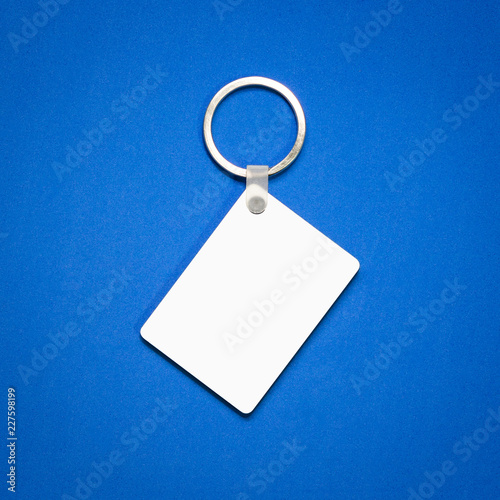 White key ring on blue background. Key chain for your design. Hanging accessory or souvenir. ( Rectangle shape )