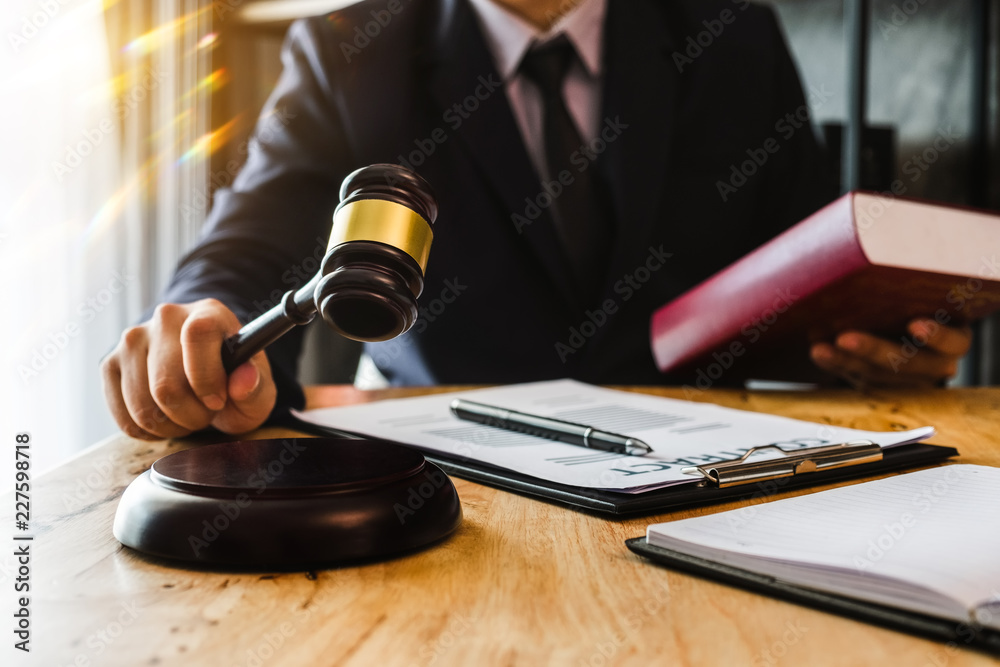 Justice and law concept.Male judge in a courtroom with the gavel, working with, digital tablet computer and smartphone docking keyboard, eyeglasses, on table in morning light Justice and law concept.Male judge in a courtroom with the gavel, working with, digital tablet computer and smartphone docking keyboard, eyeglasses, on table in morning light