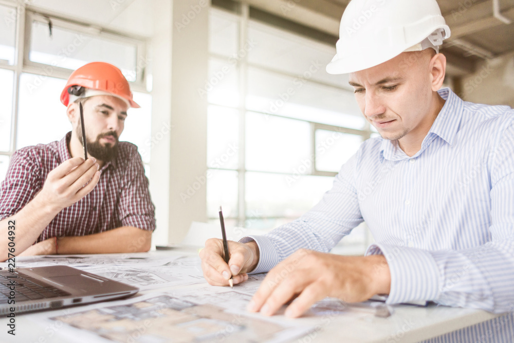 male engineers, architects working at the desk in helmets. Drawings, laptop, roulette on the desktop. Reception and supervision of building construction male engineers, architects working at the desk in helmets. Drawings, laptop, roulette on the desktop. Reception and supervision of building construction