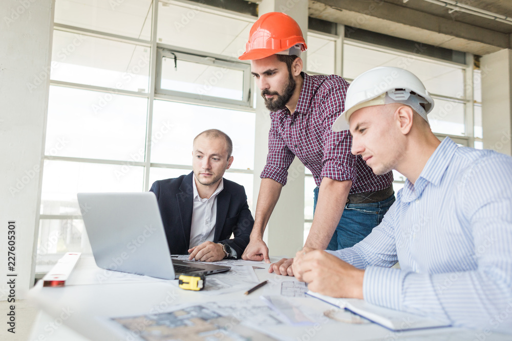 male engineers, architects working at the desk in helmets. Drawings, laptop, roulette on the desktop. Reception and supervision of building construction