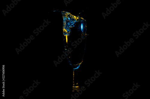 Fotografi Beverage splashing out of a tall glass under blue and yellow lights isolated on
