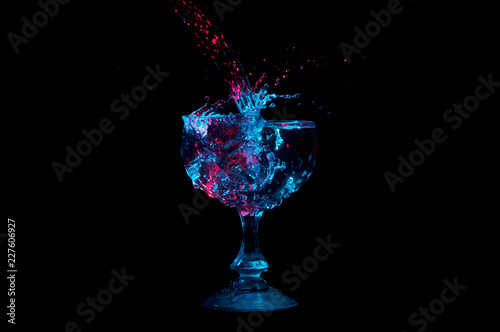 Stream of water splashing into a full glass under red and blue lights isolated on a black background