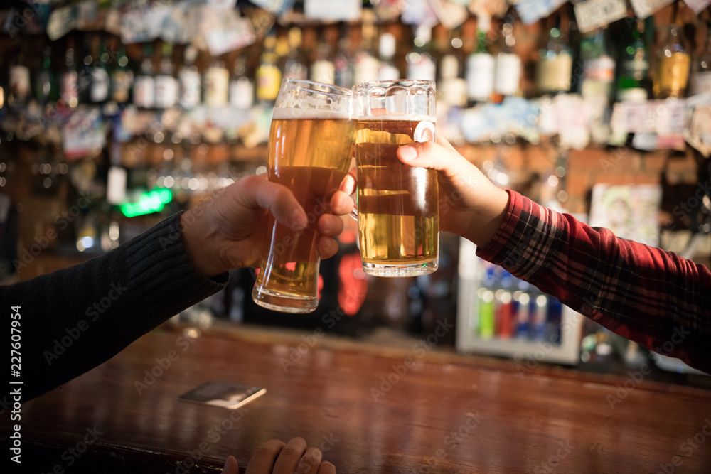 Cheers. Close-up of two men toasting with beer at the bar counter
