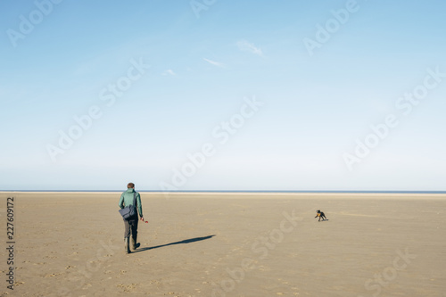 Male playing ball with his dog on a vast empty beach. Holkham, N