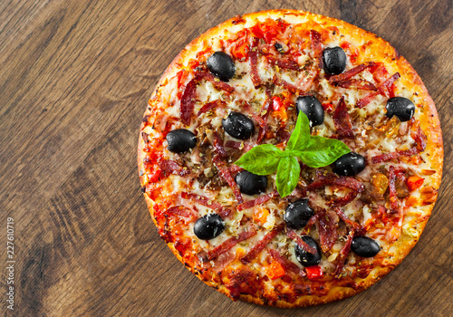 Pizza with Mozzarella cheese, salami, pepper, ham, pepperoni, olives, Spices and Fresh Basil. Italian pizza on wooden background