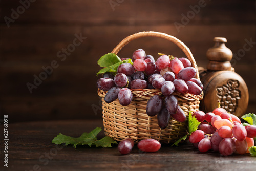 Ripe grapes in wicker basket on wooden background.