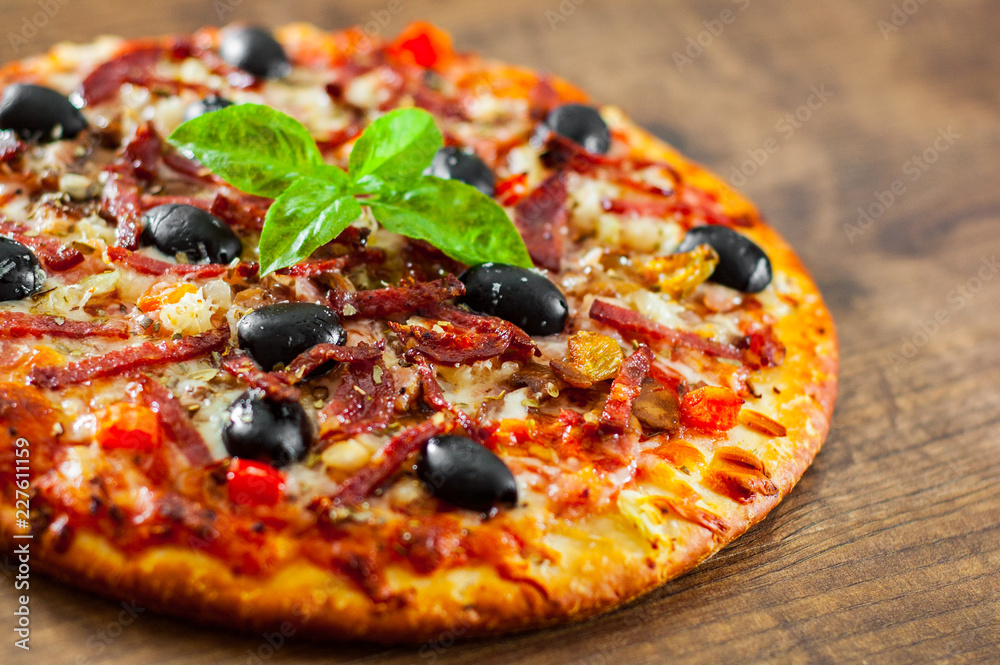 Pizza with Mozzarella cheese, salami, pepper, ham, pepperoni, olives, Spices and Fresh Basil. Italian pizza on wooden background Pizza with Mozzarella cheese, salami, pepper, ham, pepperoni, olives, Spices and Fresh Basil. Italian pizza on wooden background