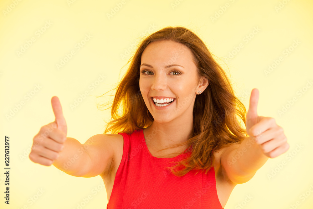 Beautiful young woman in red dress shows thumbs up as gesture for success
