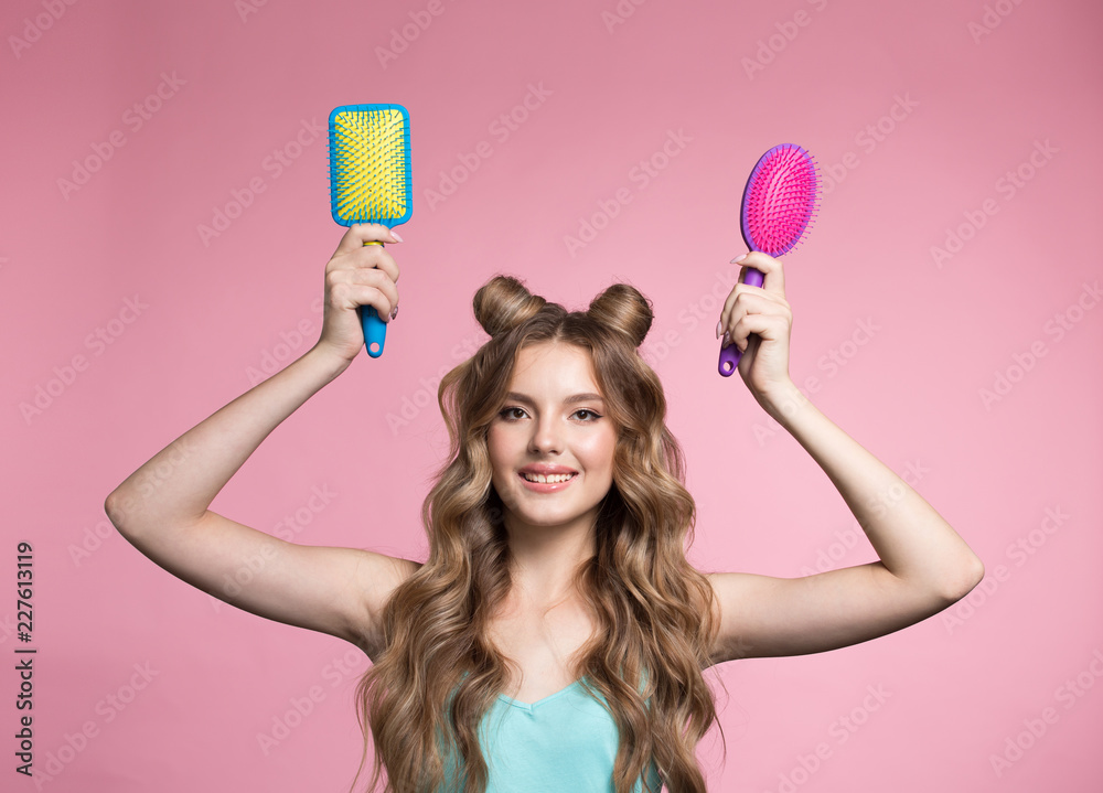 A woman holds a hairbrush in her hands. Woman on a pink background with curly long hair.