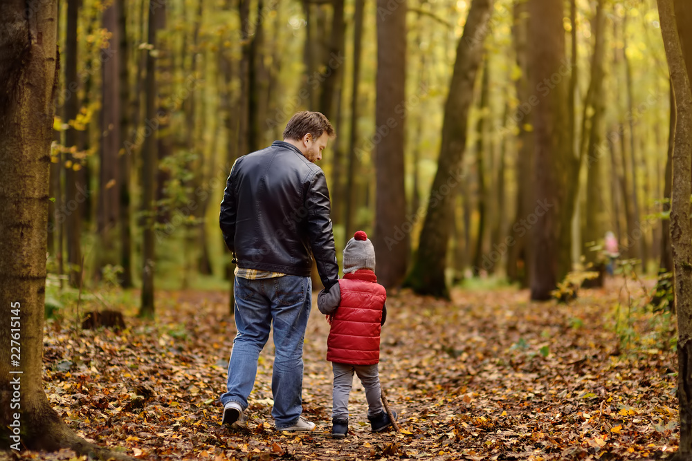 Father and his toddler son walking during the hiking activities in autumn forest at sunset