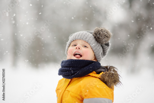 Cute little boy catching snowflakes with her tongue in beautiful winter park