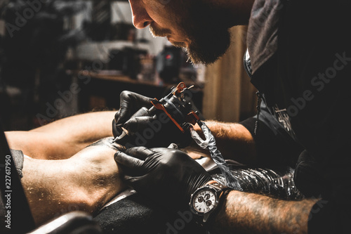 The tattoo artist creates a picture on the body of a man. close-up of tattoo machines and hands