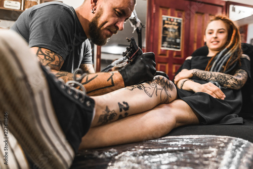 girl with dreadlocks in a tattoo parlor. The master creates a picture on the body of a young beautiful girl. Close-up of hands and tattoo machine
