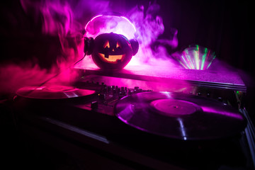 Halloween pumpkin on a dj table with headphones on dark background with copy space. Happy Halloween festival decorations and music concept