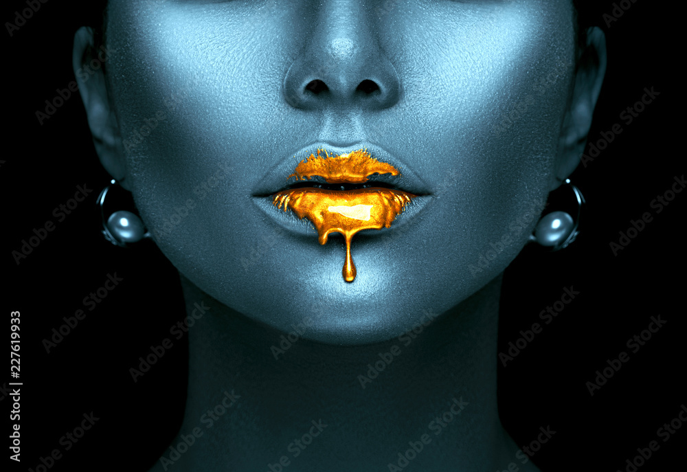 Gold paint drips from the sexy lips, golden liquid drops on beautiful model girl's mouth, creative abstract dark blue skin makeup. Beauty woman face - obrazy, fototapety, plakaty 