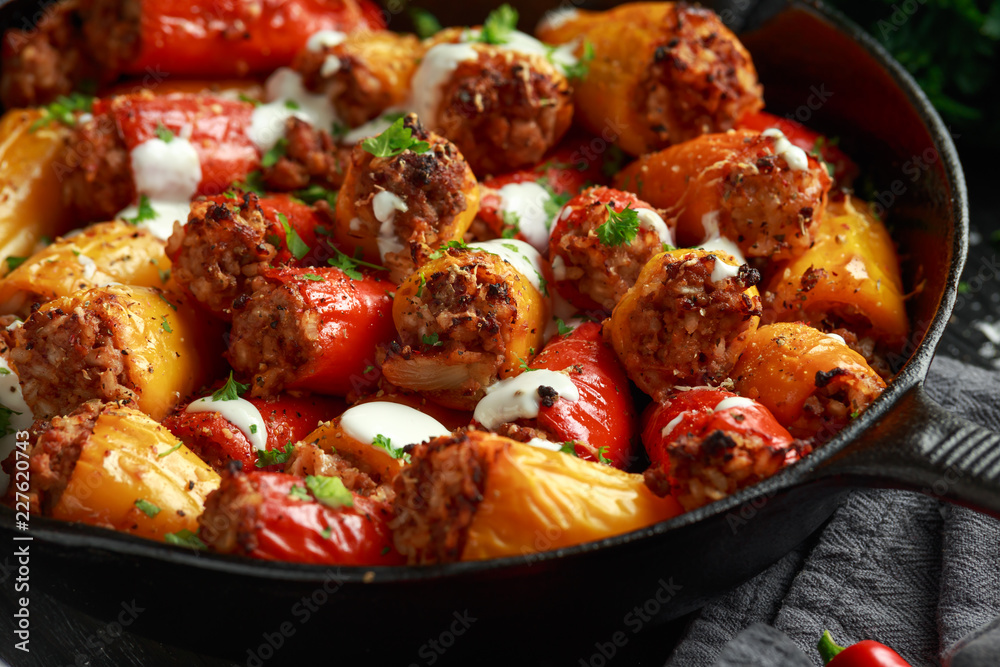 Sausage meat, mince and rice Stuffed sweet mini bell peppers baked in cast iron skillet, pan topped with yogurt and fresh parsley