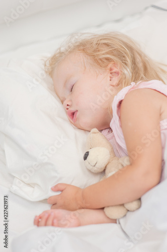 little baby girl sleeping on a bed with toy bear. Top view