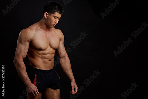 Asian tanned strong man in shorts looking down. closeup side view photo. isolated on the black background. strength and fitnesss concept photo