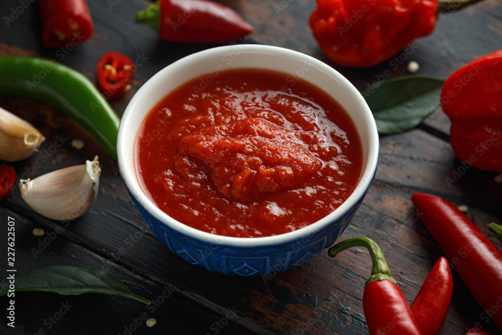 spicy hot sweet chili sauce with mix of chilli pepper, garlic and tomatoes on rustic wooden background spicy hot sweet chili sauce with mix of chilli pepper, garlic and tomatoes on rustic wooden background