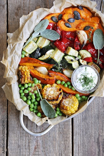 Roasted vegetables in serving pan on a rustic wooden table. Overhead view.