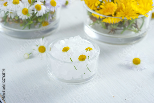 cosmetic product samples with herbal flowers on white wooden table