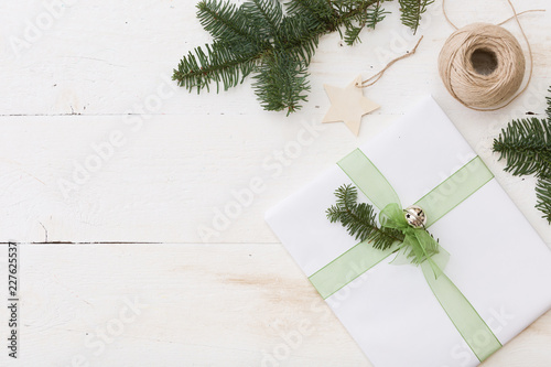 Christmas gift box with tag. New Year present in white box with fir branches at white wooden table. Flat lay with copy space. Celebration, holiday season and winter concept