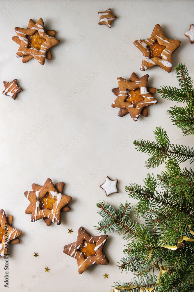Homemade Christmas star shape sugar caramel cookies with frosting and orange citrus jam over white marble background with fir branches. Flat lay, space. Sweet xmas or new year gift.