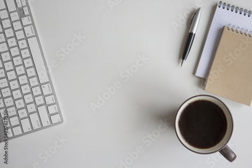 White wooden table with keyboard, earphone, pen, notebook and a cup of coffee. Workspace top view with copy space.