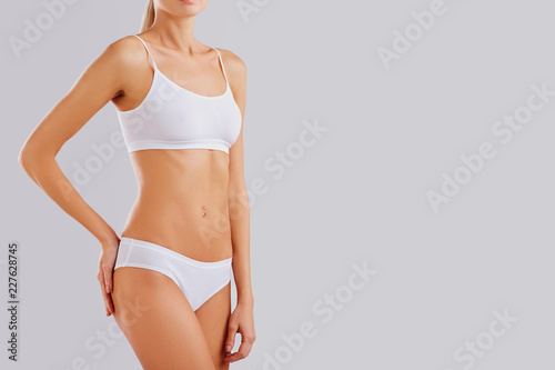 Slim body of a young woman in lingerie on a gray background.