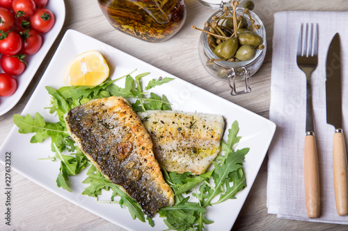 Bild auf Leinwand Grilled seabass fillet with arugula, lemon, tomatoes and capers