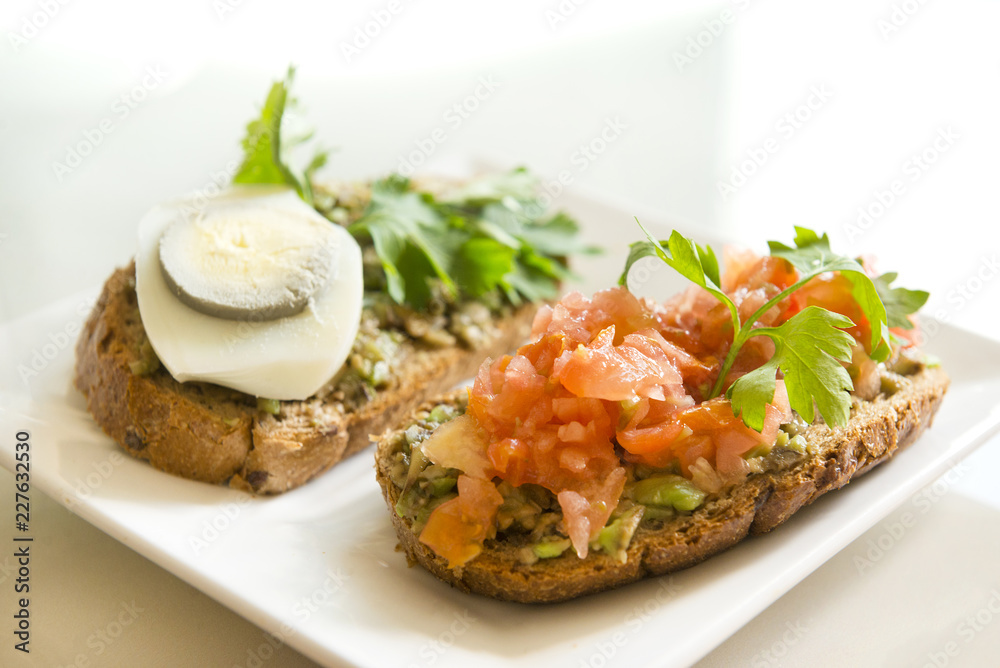 2 sandwiches with avocado, tomato, egg and herbs on a plate 2 sandwiches with avocado, tomato, egg and herbs on a plate