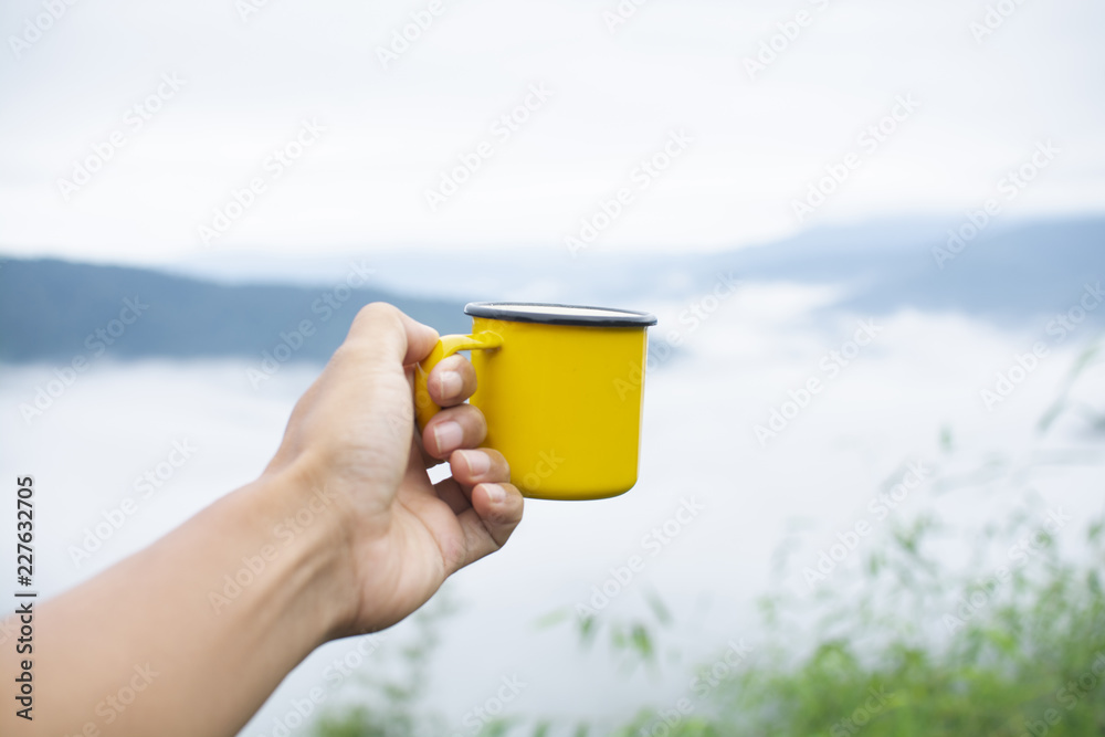 Obraz premium Hand holding yellow mug with nature background