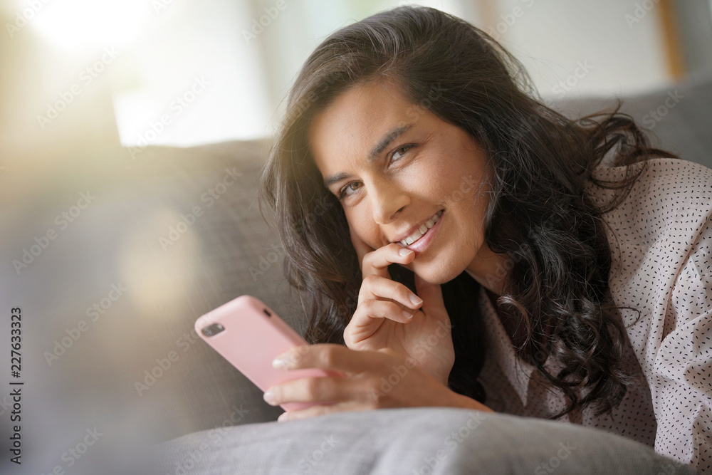 Brunette woman relaxing on sofa, connected with smartphone Brunette woman relaxing on sofa, connected with smartphone