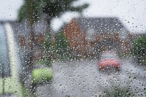 Heavy rain drops on home window glass that Look at home parked cars in hurricane weather 