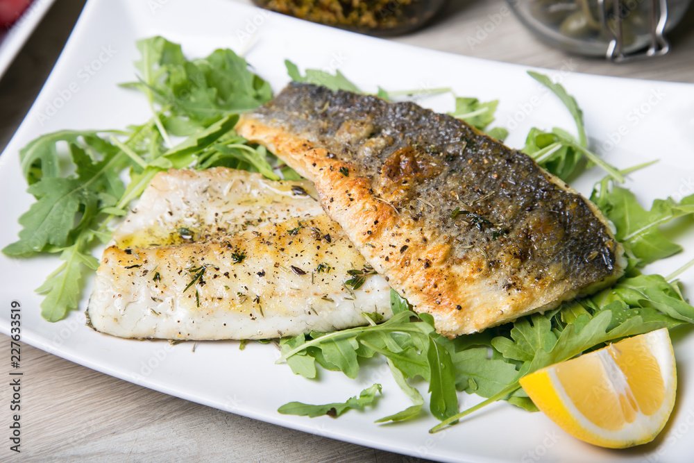 Grilled seabass fillet with arugula and lemon. Close-up. Grilled seabass fillet with arugula and lemon. Close-up.