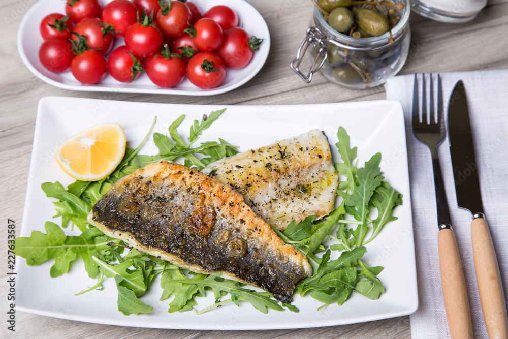Grilled seabass fillet with arugula, lemon, tomatoes and capers. Close-up. Grilled seabass fillet with arugula, lemon, tomatoes and capers. Close-up.