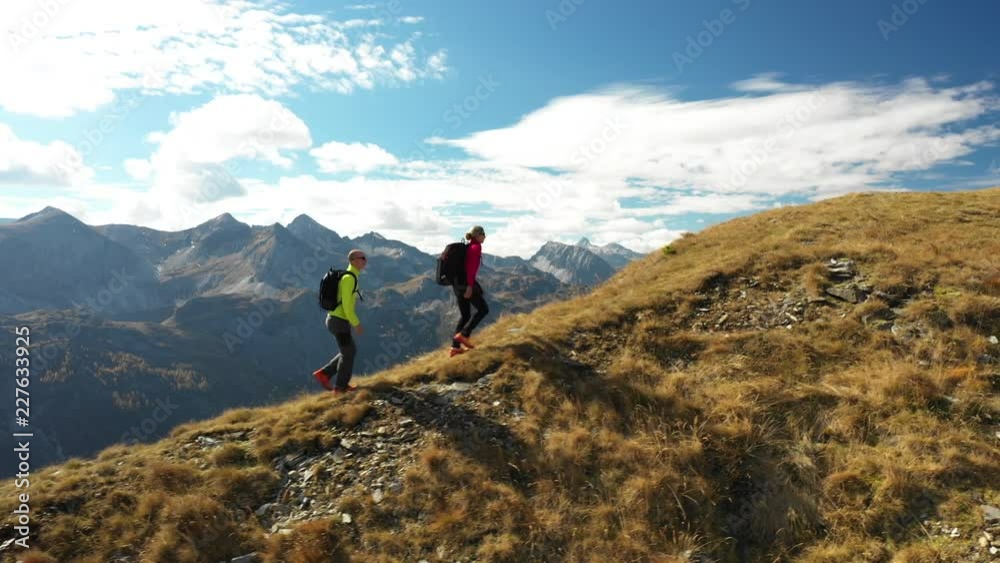 4K sport footage, aerial drone view active people couple hiking on mountain ridge on sunny day in autumn high above in middle of amazing mountains 
