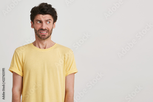 Clouse up of afraid fearful young man with dark brown hair and beard wears yellow casual tshirt, look right, standing left side isolated over white background photo
