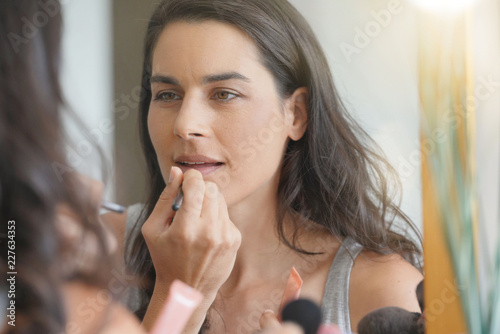 Brunette woman in front of mirror applying lipstik on